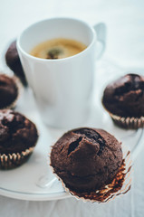 Mini chocolate muffins on white plate with a cup of coffee in the middle.
