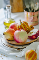 Still life with small pumpkins, apples and pears on a ceramic plate. Autumn still life in bright colors. Vegetables and fruits on the table with a white tablecloth.