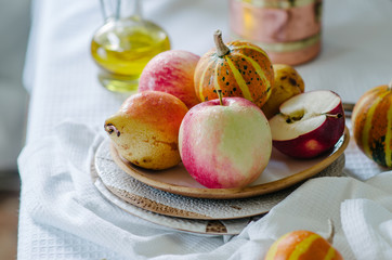 Still life with small pumpkins, apples and pears on a ceramic plate. Autumn still life in bright colors. Vegetables and fruits on the table with a white tablecloth.