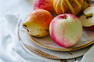 Still life with small pumpkins, apples and pears on a ceramic plate. Autumn still life in bright colors. Vegetables and fruits on the table with a white tablecloth.
