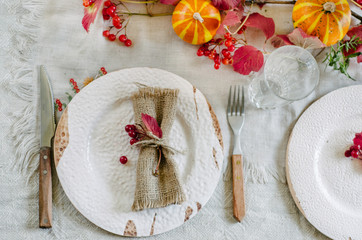 Autumn table setting with beautiful plates, pumpkins and and flowers, fall home decoration for festive dinner.