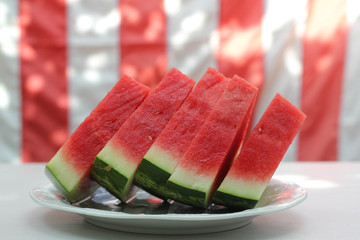 Watermelon slices in front of United States flag, outside at a summer barbecue, as for Memorial Day or the Fourth of July / Independence Day.