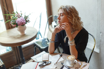 A young girl in a cafe drinks coffee and draws sketches of clothes
