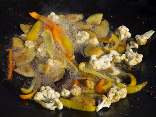 Cauliflower and peppers are fried in hot oil.