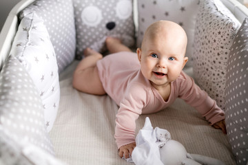 Cute, smiling baby in a pink bodysuit, lying on his stomach in a white oval bed, around light...