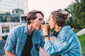 Lovely young hipster couple dating during summer sunset. they wear jeans clothes. they eat burger fastfood together