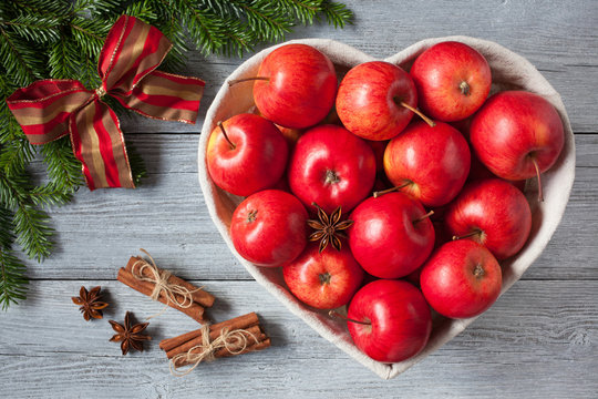 Red apples, basket in the form of heart on a wooden background, cinnamon, anise and branches of a fir