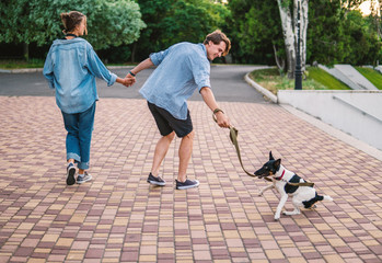 Obraz premium Lovely young hipster couple walking with dog during summer sunset. they wear jeans clothes. modern youth