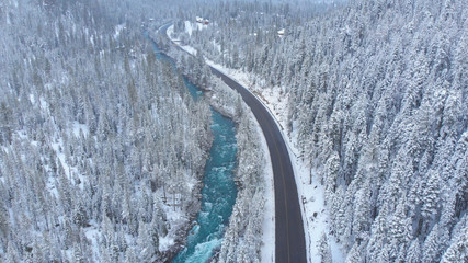 AERIAL: Flying above the picturesque winter forest and emerald colored stream.