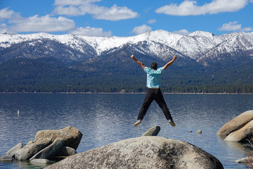 Unrecognizable man jumps off boulder with outstretched arms while at Lake Tahoe.
