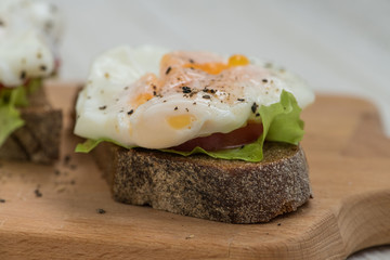 Poached eggs on a piece of rye bread with tomato and salad on a wooden cutting board