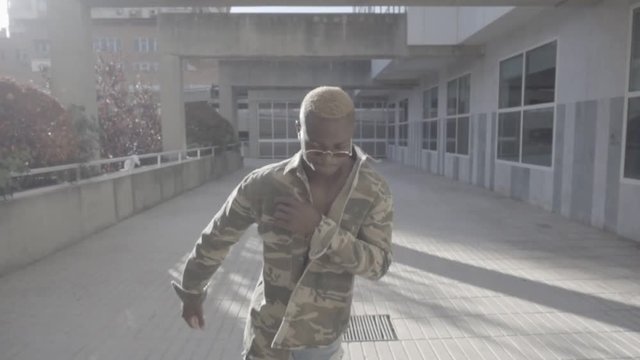 African man poses on camera dancing in city.