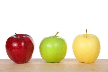 One red, green and yellow apples on a light wood table isolated on white background