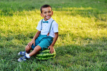 baby-cute black African American boy sitting on a huge watermelon and smiling on a Park background on a Sunny summer day