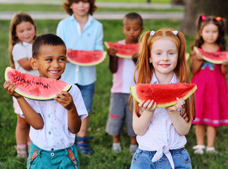 a large group of happy preschool children of different ethnic types are holding slices of ripe...