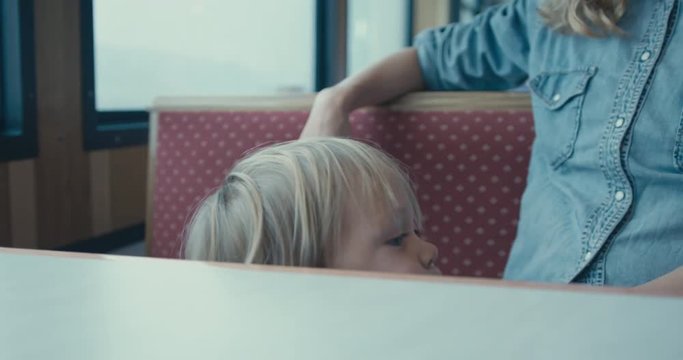 Little toddler by the window of ferry with his mother