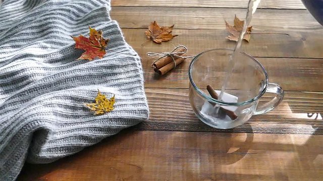 Pouring water to cup with a tea bag on a wooden table with colored autumn leaves - slow motion