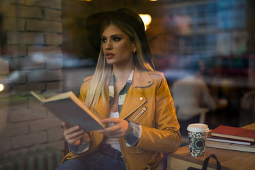 Young woman reading a book in cafe / Young woman sitting in a cafe, reading an interesting book and enjoying her coffee.