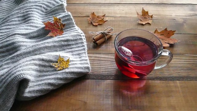 Hot Tea in clear glass cut on wooden table with autumn leaves slow motion