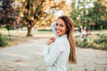 Outdoor portrait of a smiling young woman. Girl standing in the city park, looking at camera.