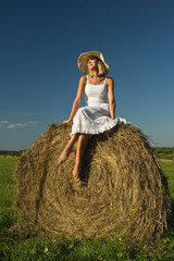 Naklejka na ściany i meble beautiful young girl at a haystack in a summer field