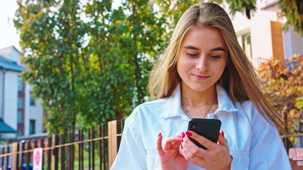 Woman texting on smartphone looking happy outside, Caucasian girl in her 20s happily texting on...