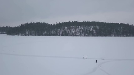 Wide aerial shot of four nature lovers enjoying the cold and crisp temperatures during a morning stroll on vast frozen lake. - Powered by Adobe