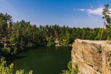 Fototapeta na wymiar Korostyshiv Canyon, deep lake in Zhytomir region with green water and blue sky in Ukraine and fir forest around