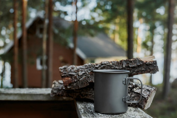 A metal mug for camping on the background of a wooden house.