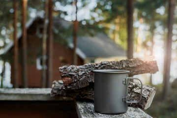 A rough metal mug on the background of chopped firewood at sunset.