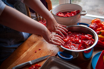 woman cook in an apron prepares tomatoes in a saucepan, rubs through a sieve and prepares tomato juice. Female hands closeup.