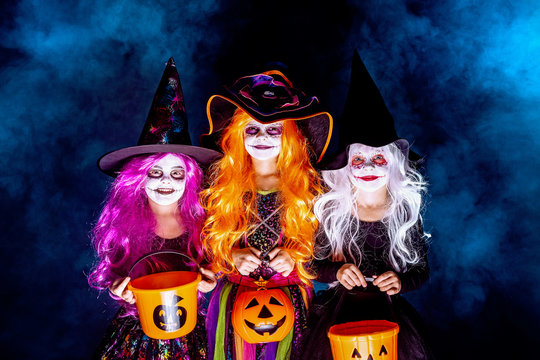 Three Beautiful girls in a witch costume on a dark background in smoke. Portrait of little girls in carnival costumes of sorceress, background on halloween. scaring and making faces .