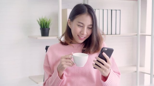 Beautiful smart business Asian woman in smart casual wear using smartphone and drinking warm cup of coffee while sitting on table in creative office. Lifestyle women working at office concept.