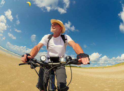 France, Bretagne, Sainte-Anne la Palud, Plage de Treguer, senior man riding mountain e-bike on beach - Powered by Adobe
