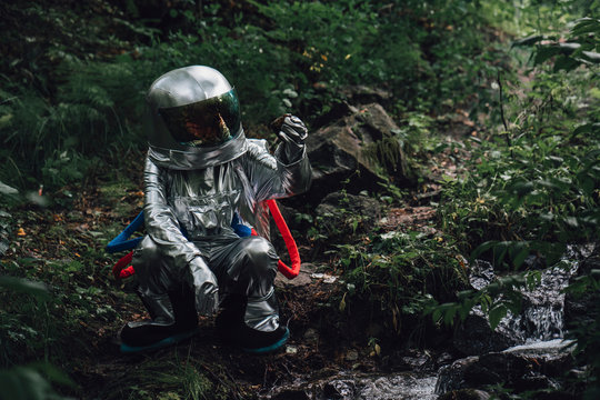 Spaceman exploring nature, crouching at a brook in forest