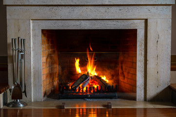 Fototapety  Wood burning in a cozy fireplace at home in interior. Fireplace as a piece of furniture. Christmas New Year concept decorations.