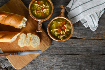 Top view of two bowls of homemade Chicken Noodle Soup with fresh baked loaf of bread
