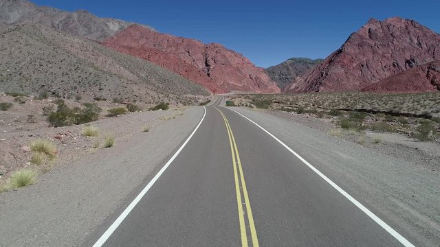 Driving throught road in a valley between colorful eroded mountains. Traveling throught desertic rocky geological formations. Catamarca, Argentina