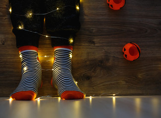 kids legs in stylish warm bright colorful striped funny socks in garland lights on floor with pumpkins in room. decor for Halloween, cosy moment. cozy autumn days. Happy Halloween celebration concept 