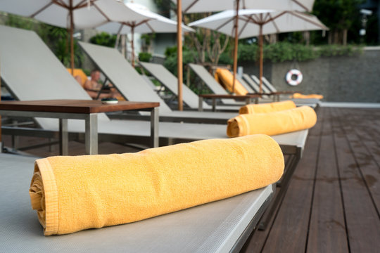 Rolled up orange towel on a sun lounger background of pool in resort or hotel.