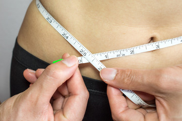 Close-up of woman measuring her waist by measure tape.