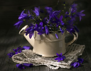 A bouquet of blue flowers in ceramic watering on wooden table.