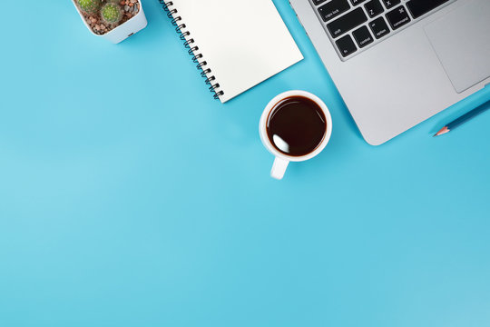 business office table with workspace, laptop computer, coffee cup, notebook, pencil, plant and cell phone on blue pastel background