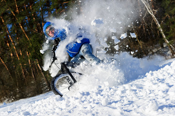 Naklejka premium Extreme cyclist riding bicycle near snowbanks of mountain slope, winter sport, cross country biking near forest in cool sunny day 
