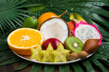 Obraz na płótnie Canvas Exotic tropical fruits plate on palm leaves and wooden background, healthy food, diet nutrition, selective focus 