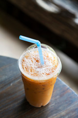 Ice Thai milk tea in plastic glass on wooden table