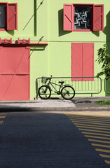 Fototapeta na wymiar Black Bike with basket standing in front of a colourful green house with red windows at Clarke Quay in Singapore