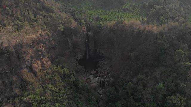 Beautiful ungraded aerial view of hills with rice field terrace and waterfall in the morning at Cimarinjung waterfall during dry season in Geopark Ciletuh, Sukabumi, Indonesia.
