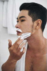 Young Asian man applying shaving foam on his face