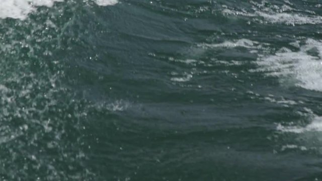Slow motion footage of water splashing off a boat's wake on a lake.